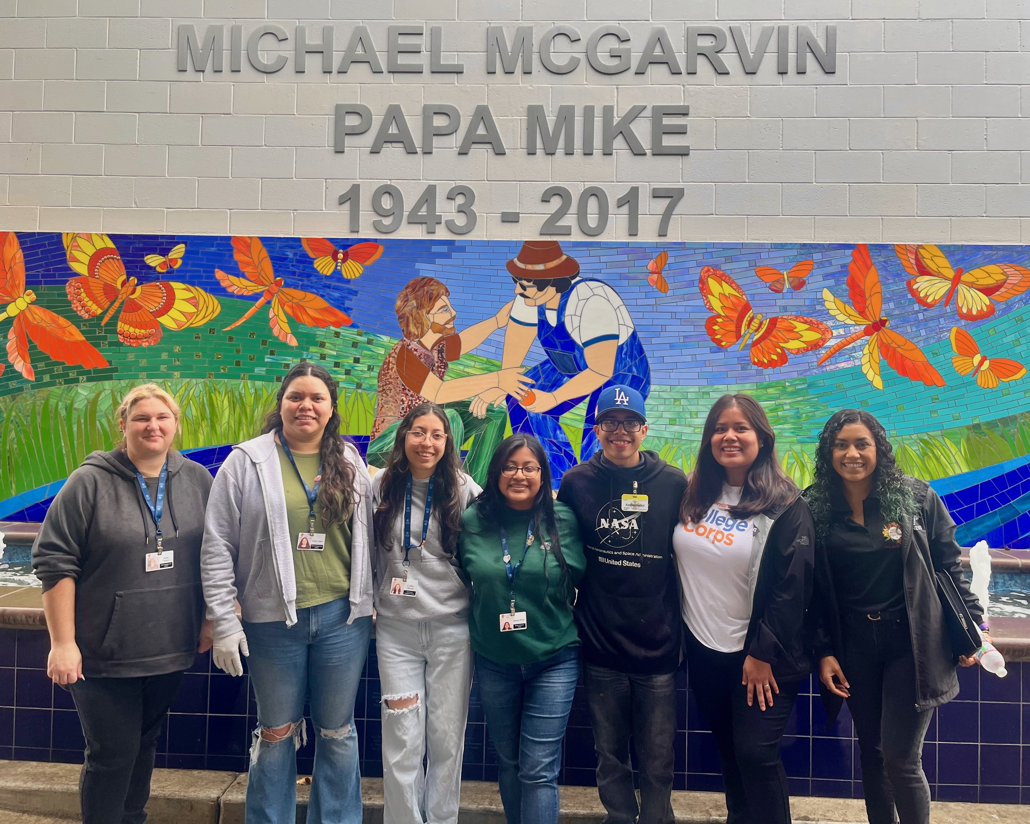 Students take a photo in front of a mural of Michael "Papa Mike" McGarvin at the Poverello House.