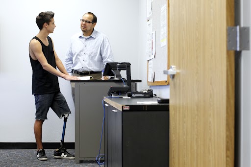 A student with a prosthetic leg and a faculty member in conversation in a classroom